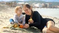 Cheerful woman with her toddler son relaxing on the sandy sea beach and having picnic. Family vacation and weekend on nature Royalty Free Stock Photo
