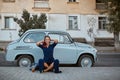 Cheerful woman posing on old fashioned car background. Lady in blue dress on street. Travel time and new place concept