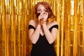 Cheerful woman with red hair wears black dress, poses over tinsel curtain, has fun at night club, covering her face with her hair Royalty Free Stock Photo