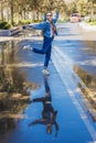 A cheerful woman stands on one leg in a dancing pose on a wet alley in the park. Mirror reflection in a puddle. Dance on Royalty Free Stock Photo