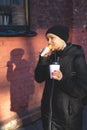 Cheerful woman in the street drinking morning coffee an d eat hot dog at winter time Royalty Free Stock Photo