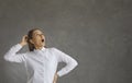 Cheerful woman with a surprised expression looks up while standing on a gray background. Royalty Free Stock Photo