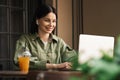 Cheerful Woman Using Earphones and Laptop While Sitting at a Cafe Table, Brunette Girl Working at Restaurant With Royalty Free Stock Photo