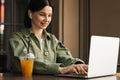 Cheerful Woman Using Earphones and Laptop While Sitting at a Cafe Table, Brunette Girl Working at Restaurant With Royalty Free Stock Photo