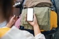 Cheerful woman using mobile phone blank white screen display frameless modern design while pack clothes a suitcase ready Royalty Free Stock Photo