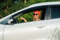 Cheerful woman in a watch cap driving in a countryside, holding coffee cup