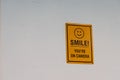 Cheerful yellow sign with an encouraging message of 'Smile, you're on camera' on a white wall