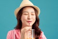 Cheerful you Asian woman drinking fruit juice and wearing straw hat, white t-shirt, short jeans, pink jacket over blue background Royalty Free Stock Photo