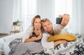 Cheerful young adults ÃÂouple in pajamas taking a Funny grimace selfie photo using a modern smartphone as they lazy relaxing lying