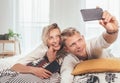 Cheerful young adults ÃÂouple in pajamas taking a selfie photo using a modern smartphone as they lazy relaxing lying in a cozy bed