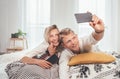 Cheerful young adults ÃÂouple in pajamas taking a selfie photo using a modern smartphone as they lazy relaxing lying in a cozy bed