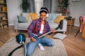 Cheerful young african american female in headphones playing at imaginary guitar as vacuum cleaner in living room Royalty Free Stock Photo