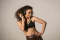 Cheerful young African-American girl listening music wearing black top and leather pants in headphones, isolated on grey Royalty Free Stock Photo