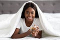 Cheerful african american woman enjoying herbal tea in bed Royalty Free Stock Photo