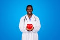 Cheerful young african american man doctor in white coat hold red heart in hands Royalty Free Stock Photo