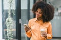 Cheerful young African American pretty woman, entrepreneur in casual wear, smiling, using smartphone in a modern office. Royalty Free Stock Photo