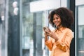 Cheerful young African American pretty woman, entrepreneur in casual wear, smiling, using smartphone in a modern office. Royalty Free Stock Photo