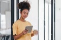 Cheerful young African American pretty woman, entrepreneur in casual wear, smiling, using smartphone in a modern office. Royalty Free Stock Photo