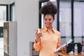 Cheerful young African American pretty woman, entrepreneur in casual wear, smiling, using smartphone in a modern office. Royalty Free Stock Photo