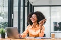 Cheerful young African American pretty woman, entrepreneur in casual wear, smiling, using smartphone and working in a Royalty Free Stock Photo