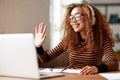 Cheerful afro american female waving at webcam on laptop, having video call while working remotely or studying online Royalty Free Stock Photo