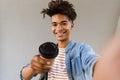 Cheerful young african guy standing outdoors holding coffee make selfie by camera