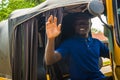 cheerful young african man driving a tuk tuk taxi smiling on a very sunny day waving to a passenger Royalty Free Stock Photo
