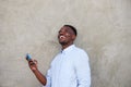 Cheerful young african man with mobile phone standing by wall Royalty Free Stock Photo