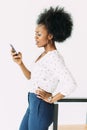 Cheerful young afro american business woman talking on cell phone, standing near the modern chair, isolated on white Royalty Free Stock Photo