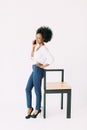 Cheerful young afro american business woman talking on cell phone, standing near the modern chair, isolated on white Royalty Free Stock Photo