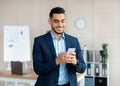 Cheerful young Arab businessman in formal sui using mobile phone, checking messages, having virtual meeting at office Royalty Free Stock Photo