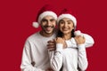 Cheerful Young Arab Couple In Santa Hats Embracing And Smiling At Camera Royalty Free Stock Photo