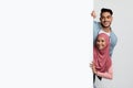 Cheerful Young Arab Couple Standing Behind White Advertisement Board And Peeking Out Royalty Free Stock Photo