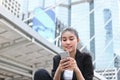Cheerful young Asian business woman with mobile smart phone in urban background. Internet of things concept Royalty Free Stock Photo