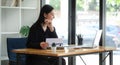 Cheerful young asian female entrepreneur sitting in bright modern office and working with computer laptop Royalty Free Stock Photo