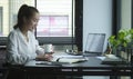 Cheerful young asian female entrepreneur sitting in bright modern office and working with computer laptop Royalty Free Stock Photo