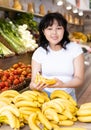 Cheerful young asian female shopper selecting ripe bananas in store Royalty Free Stock Photo