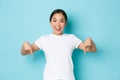 Cheerful young asian lady in white t-shirt pointing fingers down and smiling excited, looking upbeat while demontrating Royalty Free Stock Photo