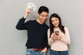 Cheerful young asian loving couple holding money and mobile phone. Royalty Free Stock Photo