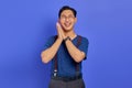 Cheerful young Asian man with hands on cheeks and wearing glasses on purple background