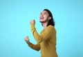 Cheerful young Asian man raising his fists with smiling delighted face, yes gesture, celebrating success on blue background