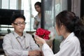 Cheerful young Asian woman accepting a bouquet of red roses from boyfriend with envious angry woman background on valentine`s day