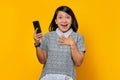 Cheerful young Asian woman holding mobile phone and putting palms on chest over yellow background Royalty Free Stock Photo