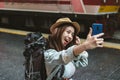 Cheerful young Asian woman traveler with backpack taking a photo or selfie in train station. Travel lifestyle concept Royalty Free Stock Photo