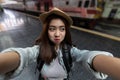 Cheerful young Asian woman traveler with backpack taking a photo or selfie in train station. Travel lifestyle concept Royalty Free Stock Photo