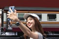 Cheerful young Asian woman traveler with backpack taking a photo or selfie in train station. Travel lifestyle concept Royalty Free Stock Photo