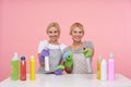 Cheerful young attractive white-headed cleaning ladies raising hands with spray bottles and looking happily at camera with broad