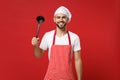 Cheerful young bearded male chef cook or baker man in striped apron toque chefs hat posing isolated on red wall