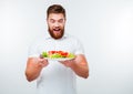 Cheerful young bearded man holding plate with fresh salad Royalty Free Stock Photo