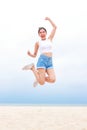 Cheerful young beautiful Asian woman having fun in white shirt and shorts jumping high on the beach. Royalty Free Stock Photo